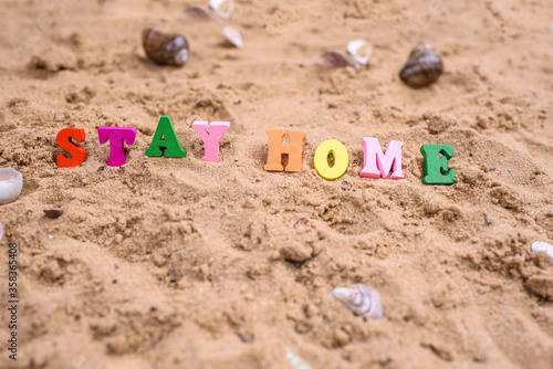 Beach sand, shells, summer, and words in wood letters stay at home.
