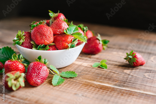 Ripe sweet strawberries in white plate on the wooden background. Copy space