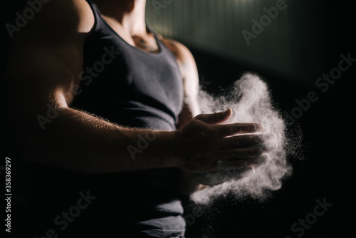 Close-up of unrecognizable strong man clapping hands with talc and preparing for workout at gym. Closeup of muscular male hands preparing for fit workout in gym with chalk magnesium carbonate.