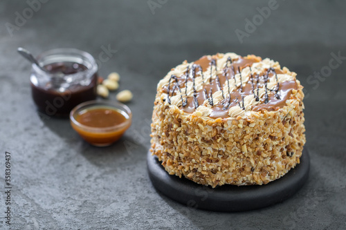 Biscuit cake with cream, caramel, nuts and chocolate on a dark background 