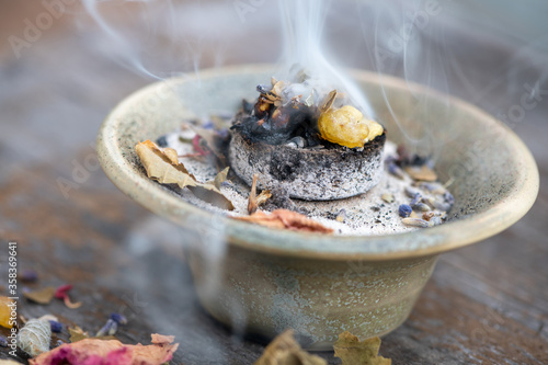 Weihrauch und getrocknete Blüten und Kräuter verbrennen bei einem Räucherritual auf einer Räucherkohle in einem Räuchergefäß mit Räuchersand  photo