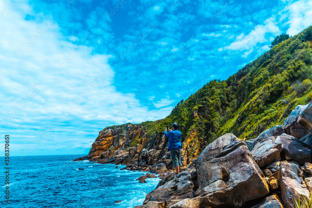 Monte Ulia in the city of San Sebastián, Basque Country. Visit the hidden cove of the city called Illurgita Senadia or Illurgita Senotia. A young man in a blue jacket in the cove taking a photo Monte Ulia in the city of San Sebastián, Basque Country. Visit the hidden cove of the city called Illurgita Senadia or Illurgita Senotia. A young man in a blue jacket in the cove taking a photo