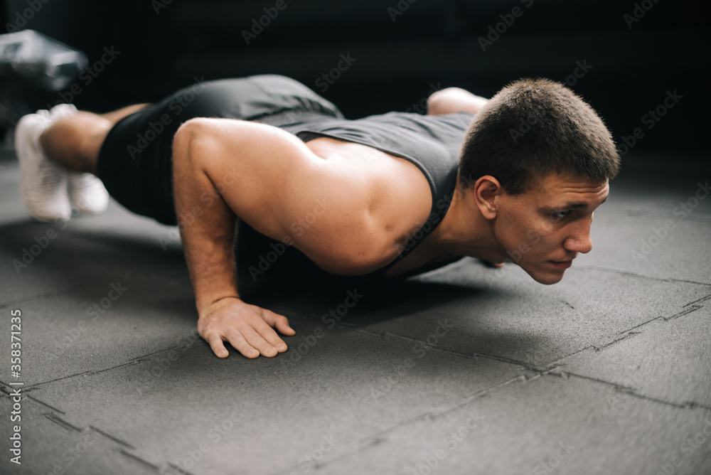 Middle shot portrait of muscular strong man doing push-ups exercise on the floor with black mats in modern dark gym. Concept of workout training in gym. Middle shot portrait of muscular strong man doing push-ups exercise on the floor with black mats in modern dark gym. Concept of workout training in gym.