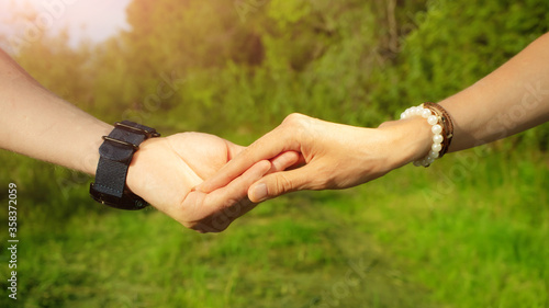 Man and woman hold hands on a background of green trees. In the frame only hands close-up. The concept of love, romance, relationship, being together, walking. Banner 16:9.