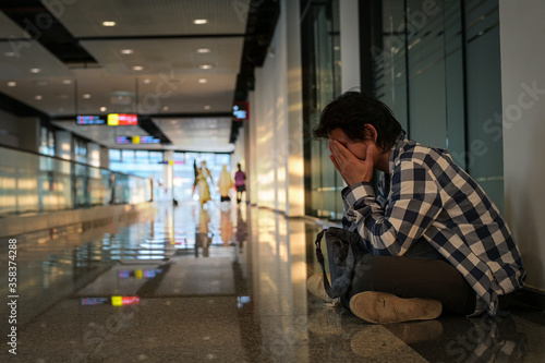 Man sitting on floor in public path way. He holding hand on head and bag feeling distress and stress because haven't been able to apply to unemployment