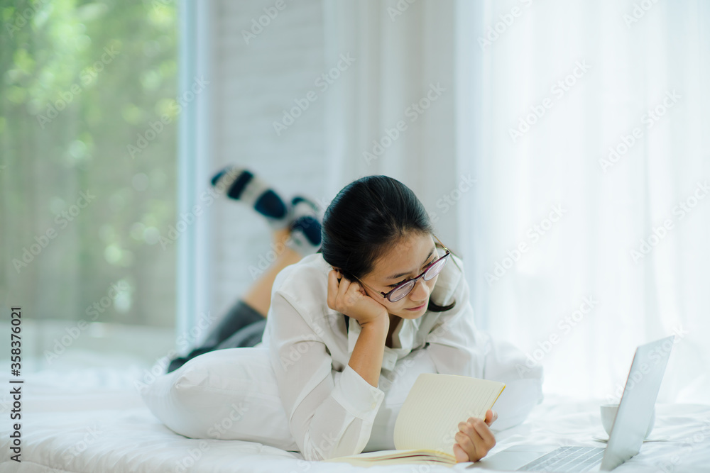 Beautiful young woman working on bed, She lecture and looking notebook. Soft and smooth focus