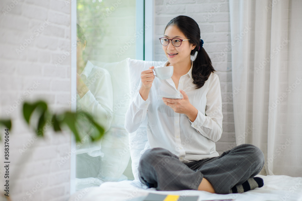 Pretty young woman sitting on bed and enjoying first morning coffee on sunshine Pretty young woman sitting on bed and enjoying first morning coffee on sunshine