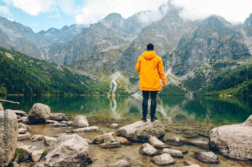 man in yellow raincoat looking at lake in mountains