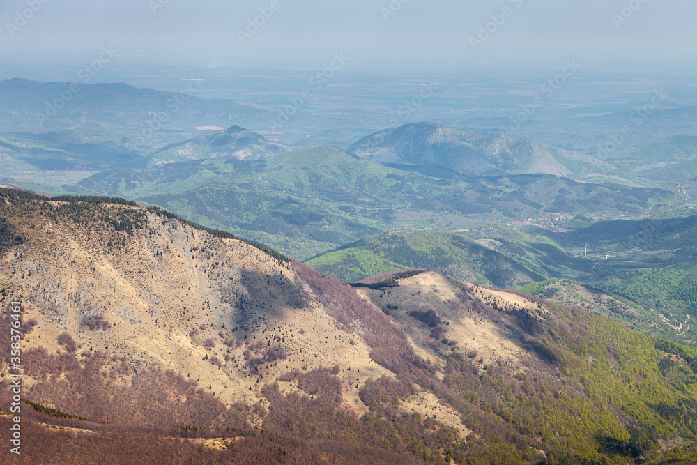 Amazing view from above of mountains covered landscape with shadows from the clouds and bright green colors of early spring colored trees