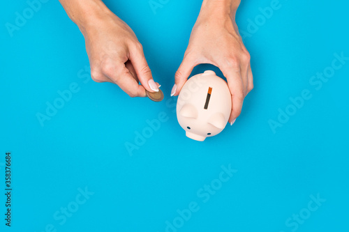 female hands put money in a piggy bank on a blue background. Savings concept. Retirement Retention