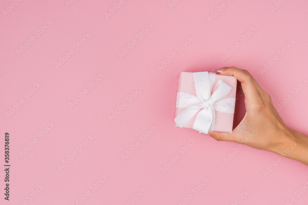 Hands holding craft paper gift box with a gift for Christmas, New Year, Valentine's Day or anniversary on a pink background, top view Hands holding craft paper gift box with a gift for Christmas, New Year, Valentine's Day or anniversary on a pink background, top view