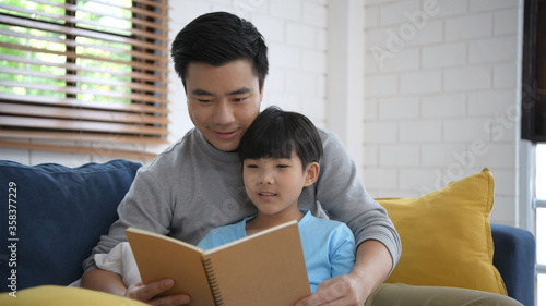 Family concept. Father teaching his son to read a book in the house. 4k Resolution.