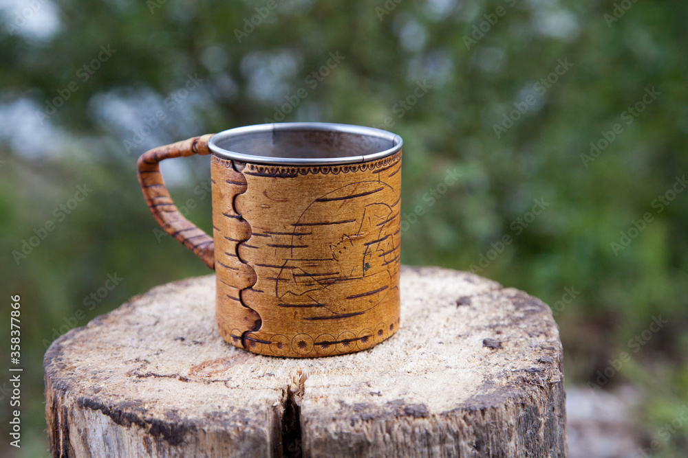 On a log is a steel mug with birch bark trim. On a log is a steel mug with birch bark trim.