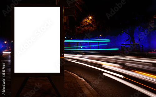 Blank electronic billboard with copy space for your text message or promotional content, public information board in the big city at night, clear poster with movement of cars on the background