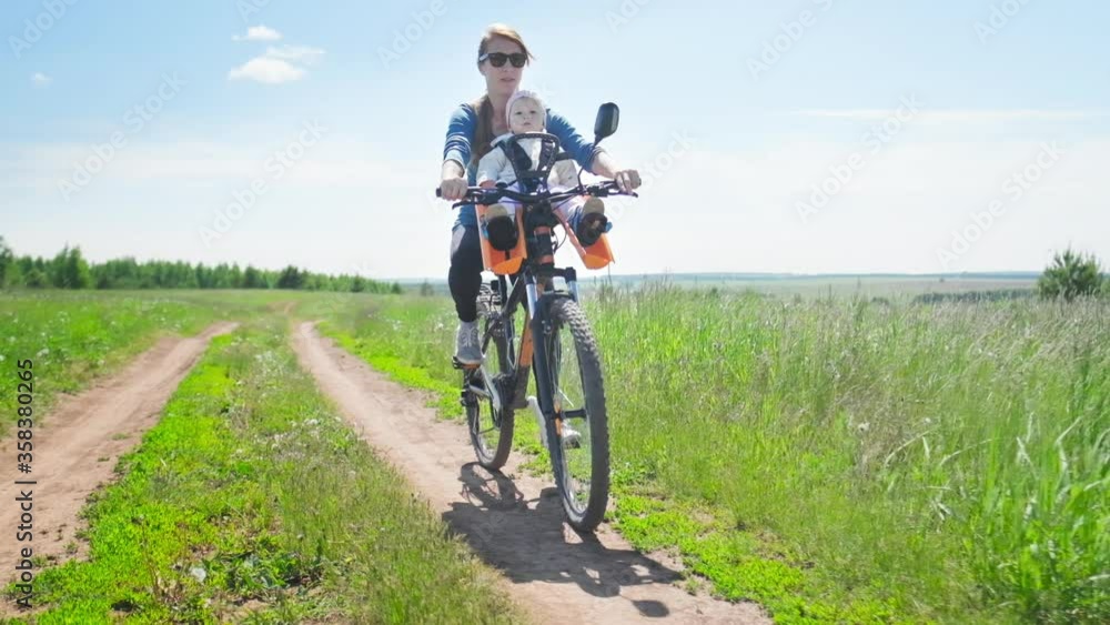Family cycling. Woman riding bicycle with baby on the front seat on a rural road and summer green meadow Family cycling. Woman riding bicycle with baby on the front seat on a rural road and summer green meadow