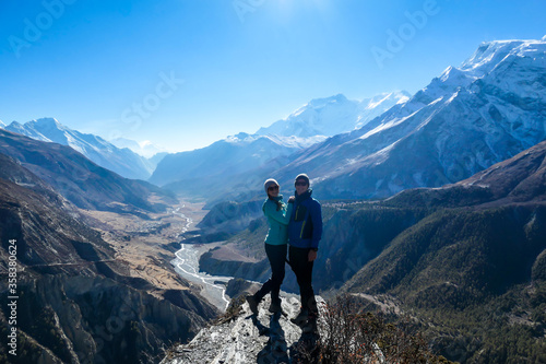 A couple standing at a mountain ledge, hugging and enjoying the view on Manang valley stretching in Himalayas, along Annapurna Circuit. Freedom. Love and passion. Snow capped Himalayas around. © Chris