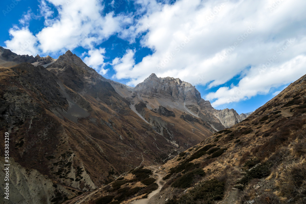 Harsh and golden colored slopes in Manang Valley, Annapurna Circus Trek, Himalayas, Nepal, with the view on Annapurna Chain and Gangapurna. Dry and desolated landscape. High snow capped mountain peaks