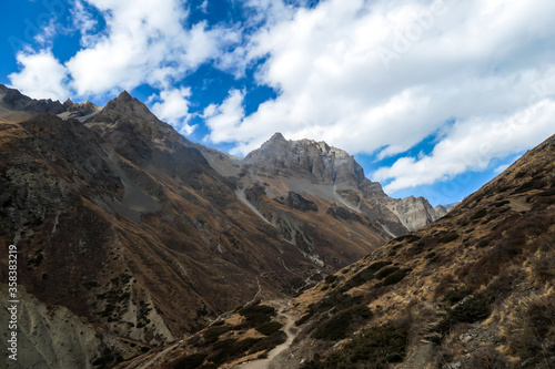 Harsh and golden colored slopes in Manang Valley, Annapurna Circus Trek, Himalayas, Nepal, with the view on Annapurna Chain and Gangapurna. Dry and desolated landscape. High snow capped mountain peaks