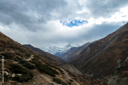 Harsh and golden colored slopes in Manang Valley  Annapurna Circus Trek  Himalayas  Nepal  with the view on Annapurna Chain and Gangapurna. Dry and desolated landscape. High snow capped mountain peaks