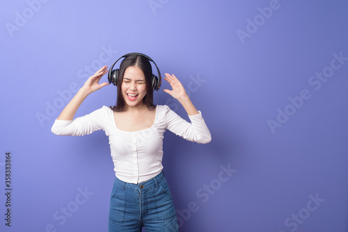 Young woman is listening to music on purple background