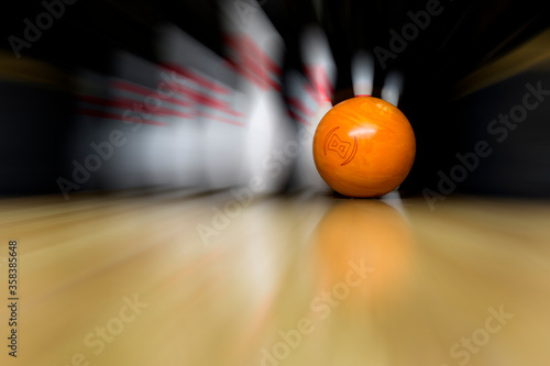 An orange bowling ball is rolling at great speed into white skittles