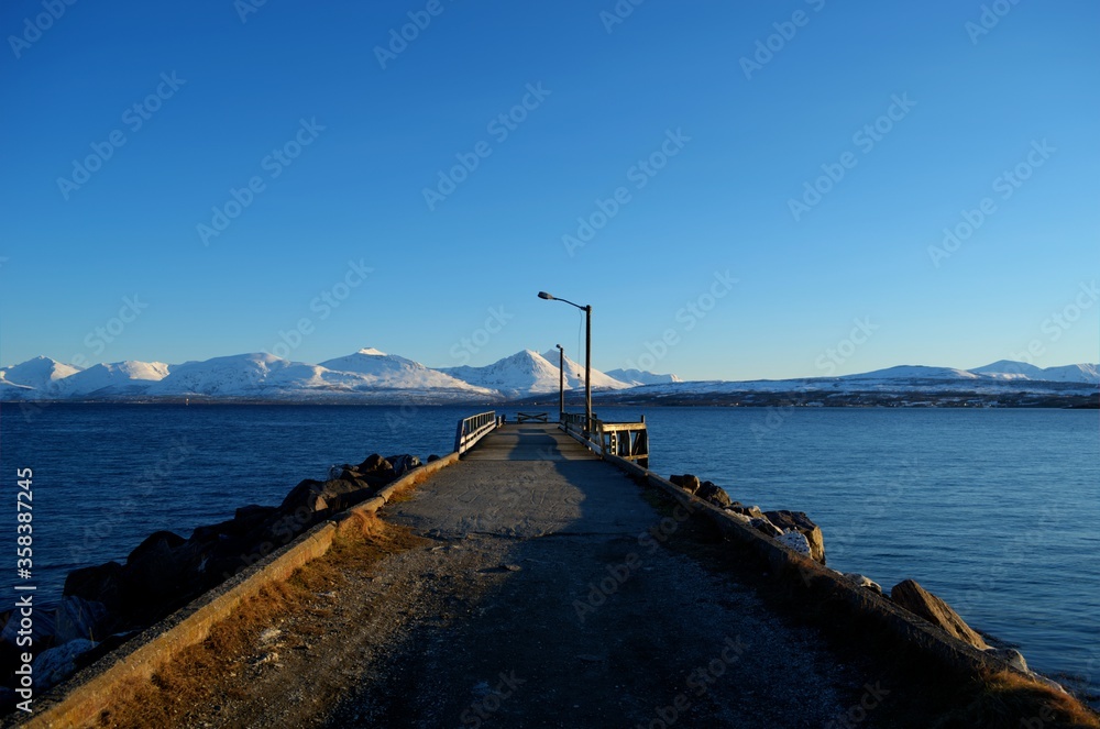 long beautiful pier with snowy mountain and blue fjord