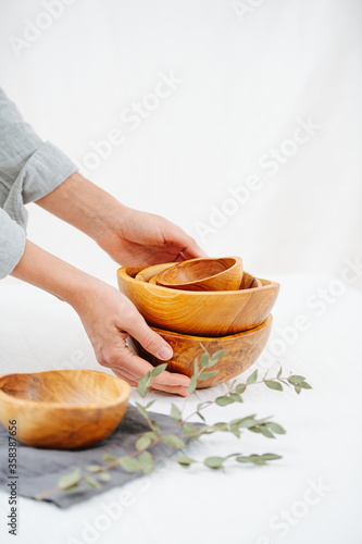 Woman hands placing stack of handmade wooden bowls on a white surface