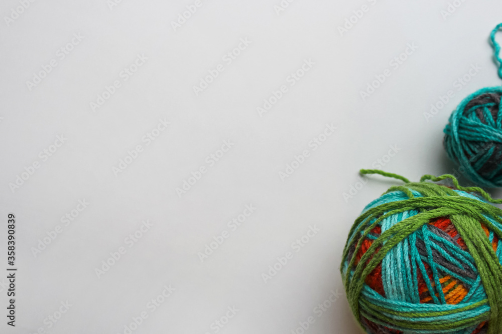 Two balls of yarn of different sizes on a white background in the corner. Large and small skein of woolen multi-colored threads. Place for text. Hobby and needlework lettering texture