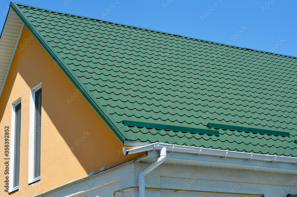 Broken roof gutter. A closeup on metal tiled gable roof with snow