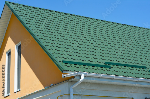 Broken roof gutter.  A close-up on metal tiled gable roof with snow stoppers, broken rain gutter system and attic windows of a house.