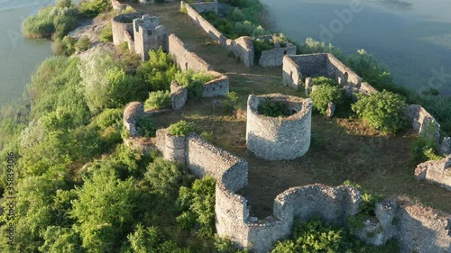 Medieval fortress on a lake island - ancient defense walls of a castle surrounded by lush green vegetation. Lesendro stronghold fortification on Lake Skadar in Montenegro. photo