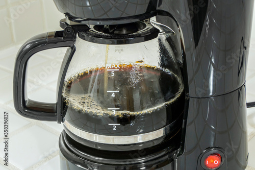 Close up of coffee maker filling pot with fresh brewed caffeine.