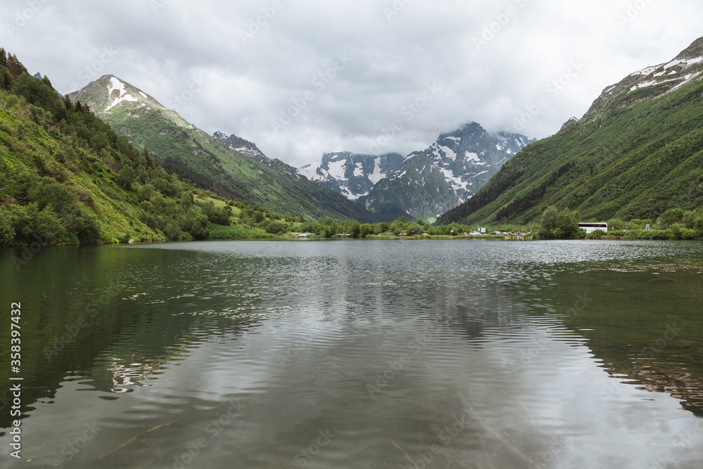 Ripple reflection in the alpine lake Tumanly Kol' with high snowy peaks and storm clouds in the background, Teberda Nature Reserve in Caucasus Mountains