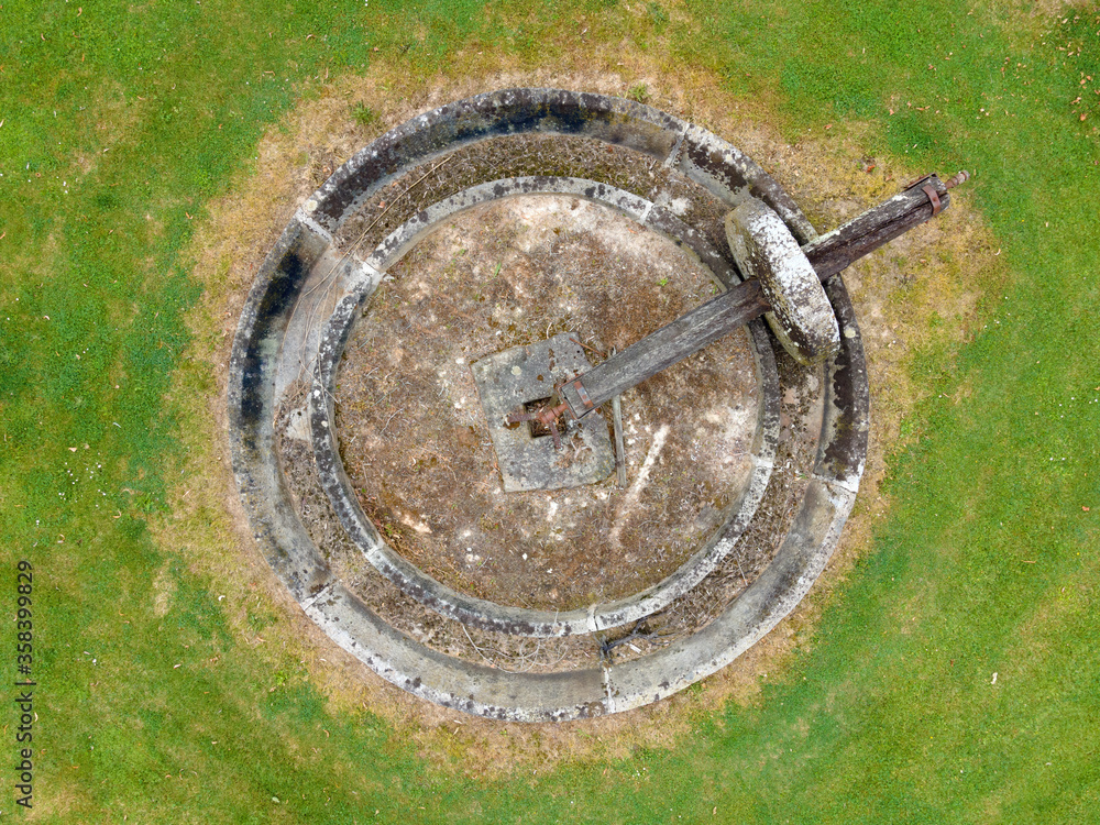 aerial view of a circular ancient millstone with a wooden axis on green grass backgroud