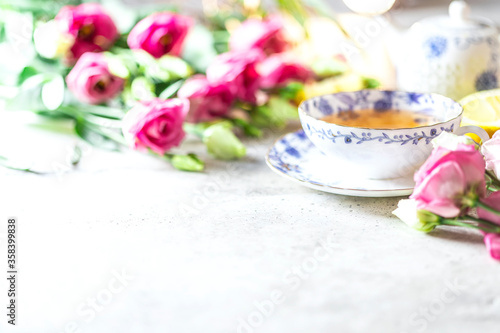 Porcelain cup of herbal green tea, lemon, mint and flowers on light grey background.