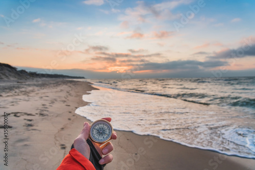 First-person view of a female hand with a compass on a background of a beautiful sea landscape. The concept of navigating the search for your own path and orientation to the cardinal points photo