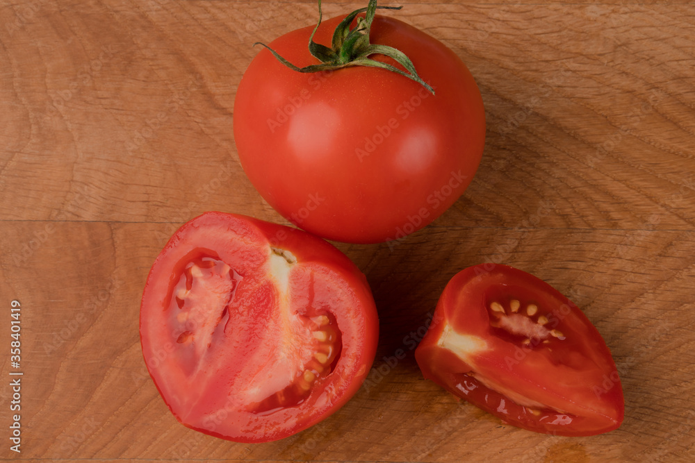 Whole tomato and pieces on a wooden board Whole tomato and pieces on a wooden board