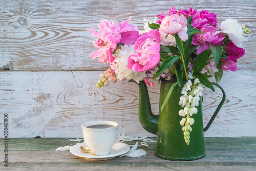 Fototapeta Naklejka Na Ścianę i Meble -  Romantic greeting card with cup of coffee and bouquet of peonies in vintage green coffee pot on white paint wooden background