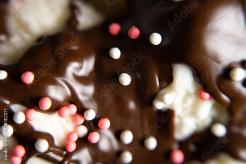 macro photo white ice cream poured with chocolate topping with sprinkles.