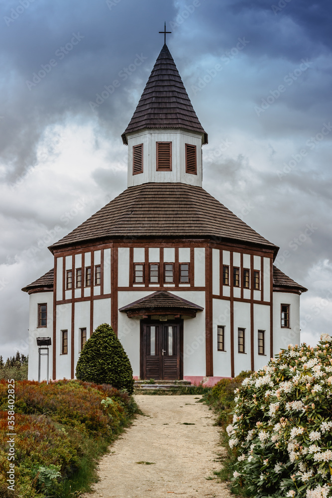 Small white Tesarovska chapel in the village of Korenov, Jizera mountains, Czech Republic. View of spring fresh landscape with blooming rhododendron.Wooden historic church