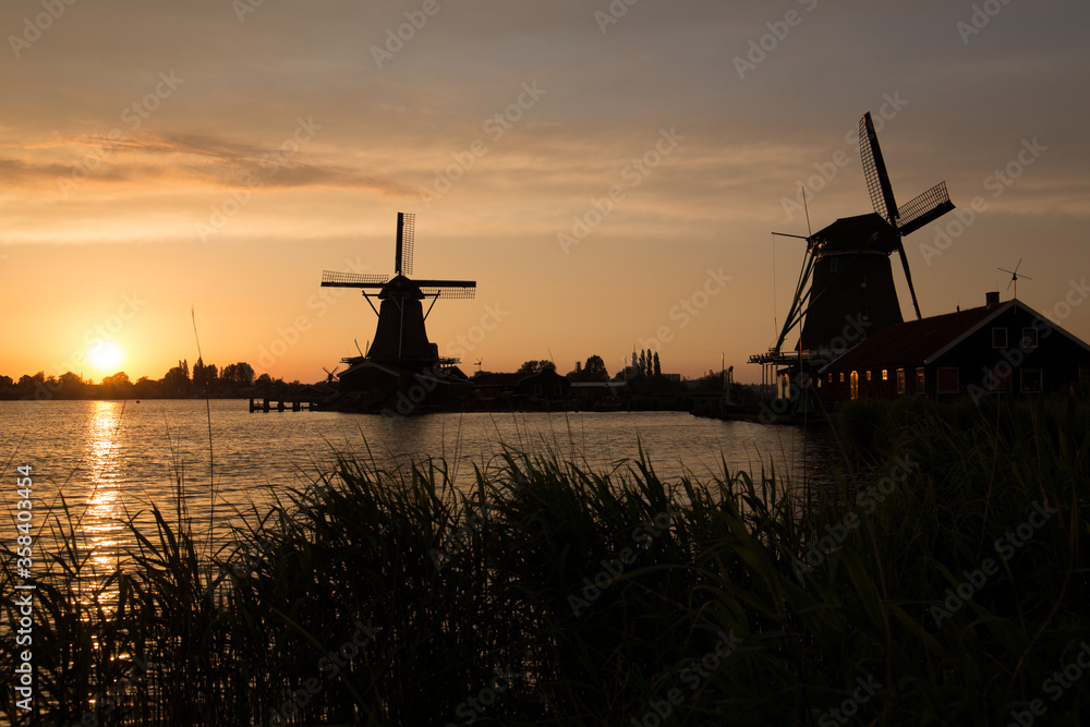 Dutch windmill silhouettes near a lake on a summer's evening with golden skies 