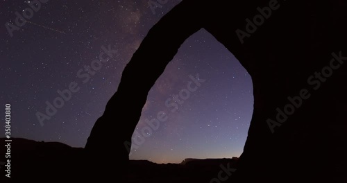 Lockdown time lapse shot of silhouette Corona Arch in desert against constellation at night - Arches National Park, Utah photo