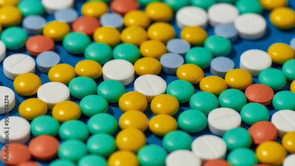 Different colorful pills scattered, lying randomly over blue background. Health care and treatment concept. Different colorful pills scattered, lying randomly over blue background. Health care and treatment concept.