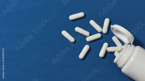 White pills, capsules scattered from a white bottle, jar on a blue background. Health care and treatment concept