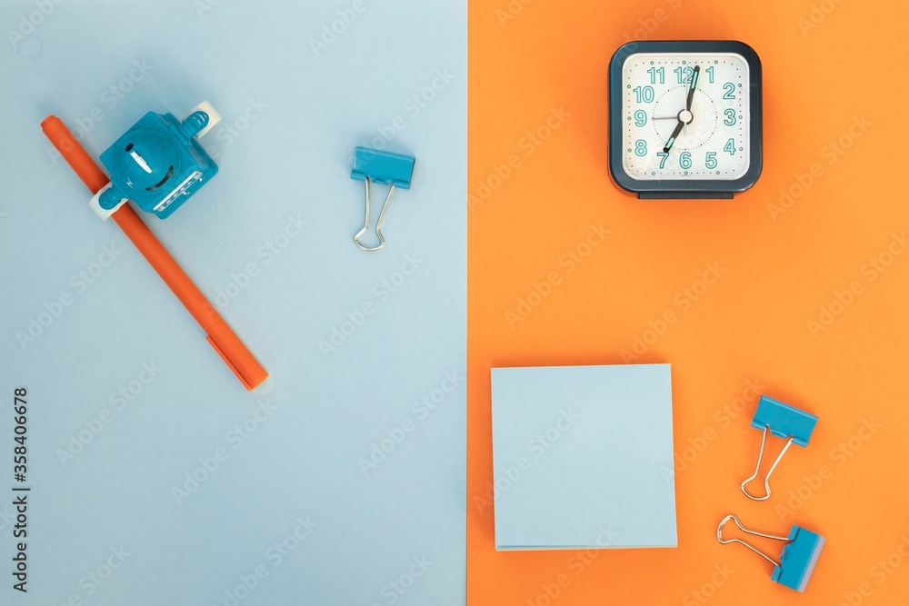 Minimum set of school and office supplies on bright blue (turquoise) and orange background: pen, clips, note paper, alarm. concept: back to school. Flatlay, top view, long banner. Minimum set of school and office supplies on bright blue (turquoise) and orange background: pen, clips, note paper, alarm. concept: back to school. Flatlay, top view, long banner.