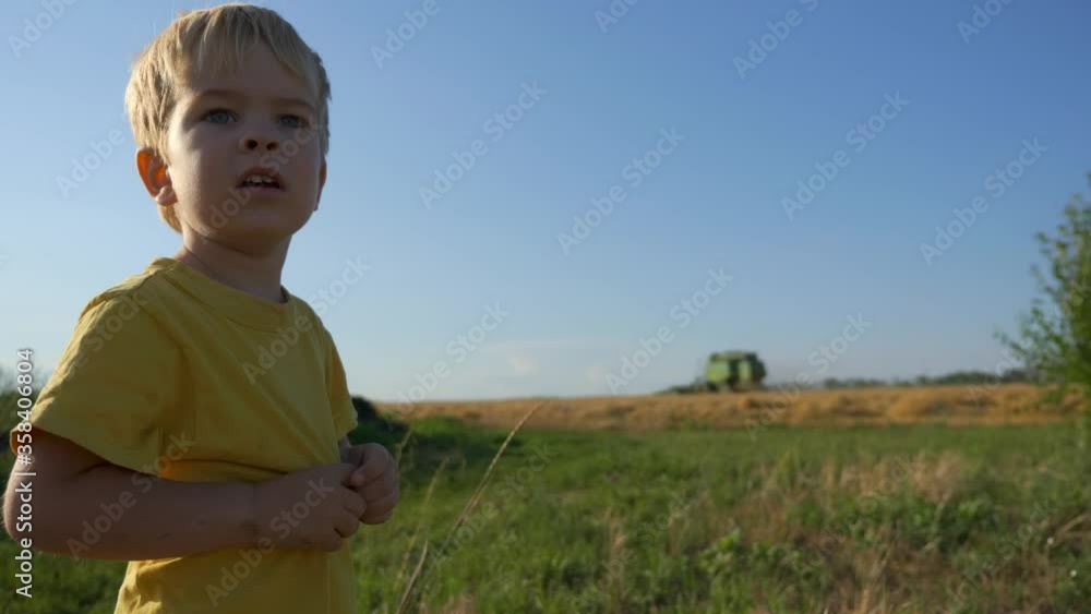 Little Boy Watching Combine Harvester in Action Working on Wheat Field Little Boy Watching Combine Harvester in Action Working on Wheat Field