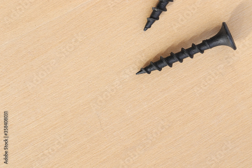 Macro photo of sharp black wood screw on plywood table background.