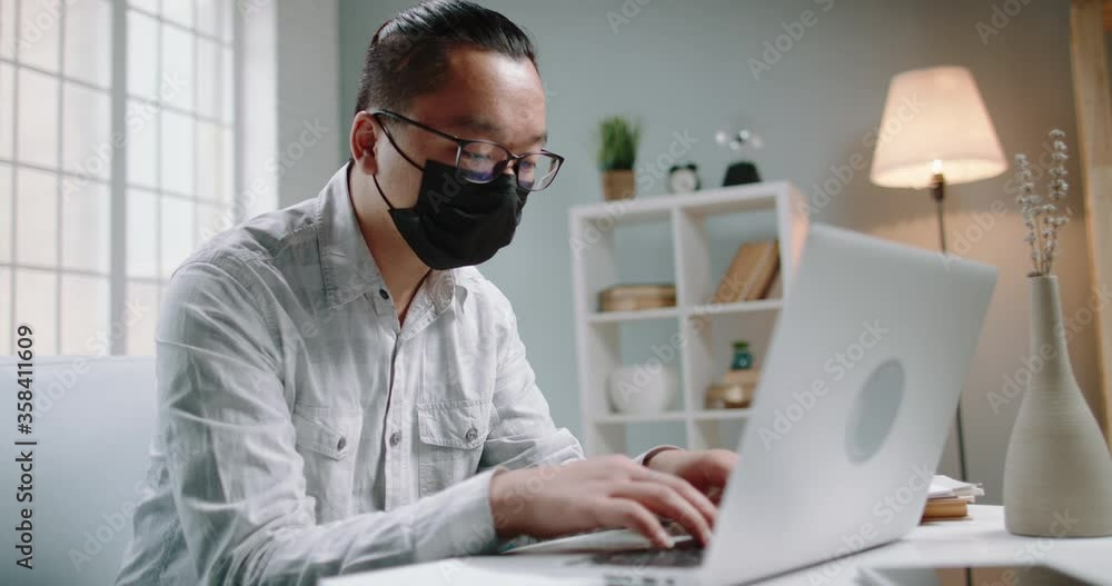 Young male chinese university student sheltering from viruses and infections at home, working at his laptop on unfinished project. Man wearing a mask to protect himself from disease 4k footage Young male chinese university student sheltering from viruses and infections at home, working at his laptop on unfinished project. Man wearing a mask to protect himself from disease 4k footage