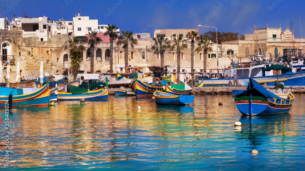 Marsaxlokk village and traditional boats reflected in the sea at sunset on the harbour of Malta