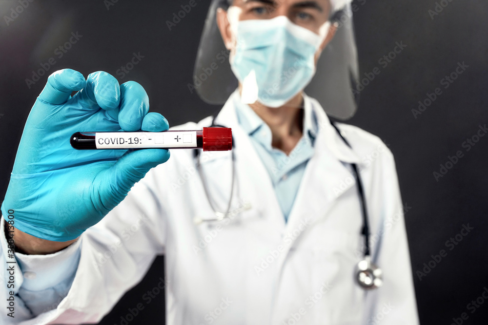 Doctor in medical mask and face shield showing test tube with blood for COVID-19 test at camera. Main focus on a test tube. Cropped shot Doctor in medical mask and face shield showing test tube with blood for COVID-19 test at camera. Main focus on a test tube. Cropped shot
